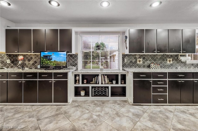 kitchen featuring dark brown cabinets, decorative backsplash, and light stone countertops