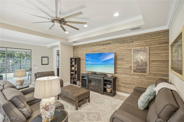 living room with ornamental molding, wooden walls, ceiling fan, and a tray ceiling