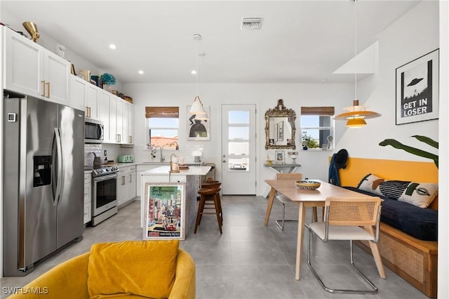 kitchen with a kitchen bar, appliances with stainless steel finishes, decorative backsplash, decorative light fixtures, and white cabinets