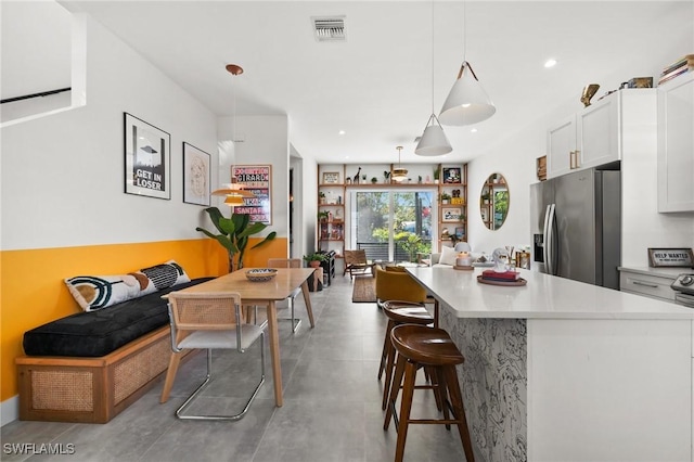 kitchen with a breakfast bar area, stainless steel fridge with ice dispenser, white cabinets, and hanging light fixtures