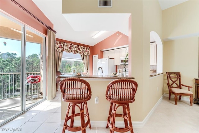 kitchen featuring white appliances, white cabinetry, kitchen peninsula, vaulted ceiling, and a breakfast bar area