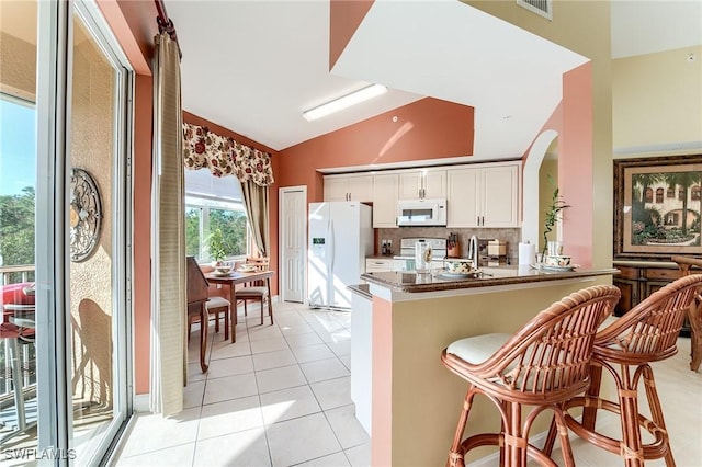 kitchen featuring white cabinetry, kitchen peninsula, white appliances, dark stone counters, and vaulted ceiling