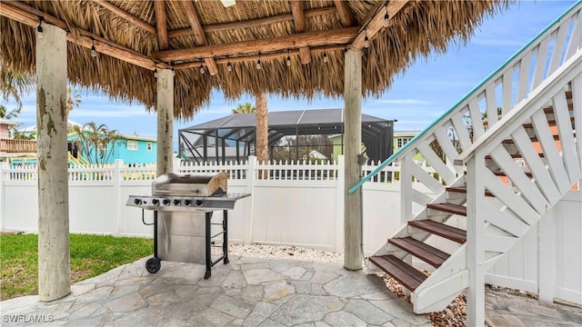 view of patio with glass enclosure, fence, grilling area, and stairs