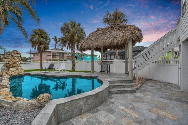 pool at dusk with area for grilling and a patio area