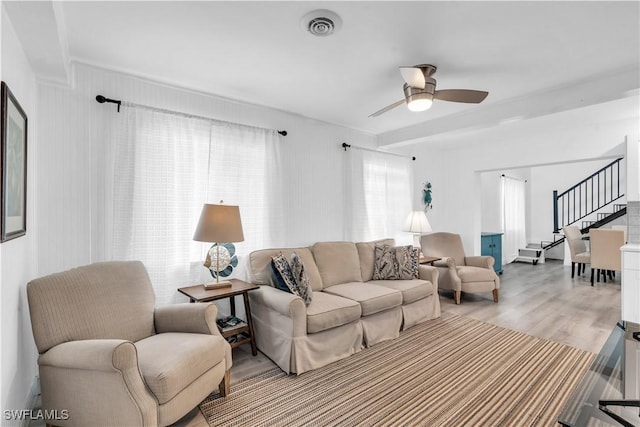 living area featuring visible vents, ceiling fan, light wood finished floors, and stairs