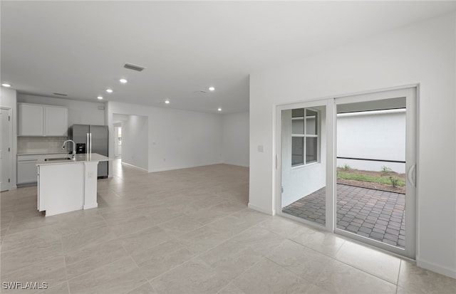 kitchen featuring sink, tasteful backsplash, a kitchen island with sink, white cabinetry, and stainless steel fridge