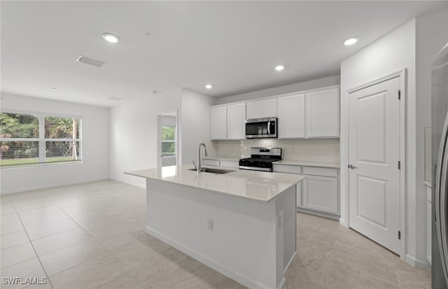 kitchen with stainless steel appliances, sink, light tile patterned floors, a kitchen island with sink, and white cabinetry