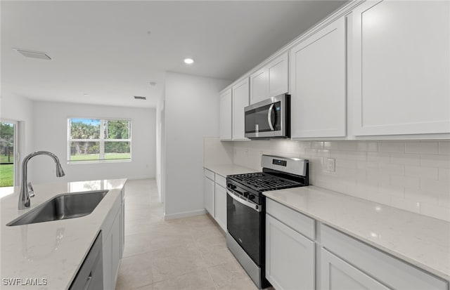 kitchen featuring stainless steel appliances, white cabinetry, sink, and light stone counters