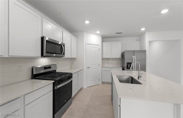 kitchen featuring stainless steel appliances, sink, an island with sink, light stone countertops, and white cabinetry