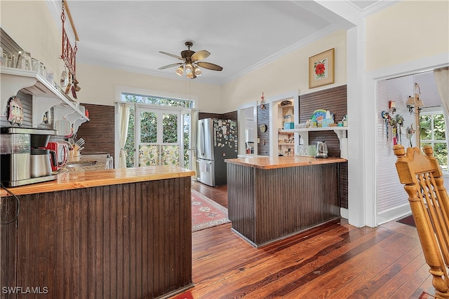 kitchen with a healthy amount of sunlight, kitchen peninsula, dark wood-type flooring, and stainless steel refrigerator