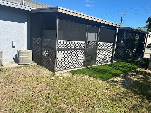 view of side of home featuring a lawn, a sunroom, and cooling unit