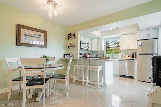 kitchen with white cabinets, light stone countertops, appliances with stainless steel finishes, kitchen peninsula, and a breakfast bar area