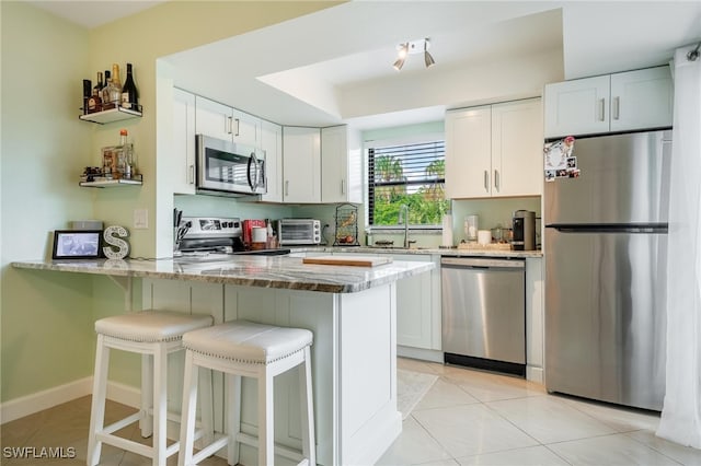 kitchen featuring white cabinets, appliances with stainless steel finishes, kitchen peninsula, and light stone counters