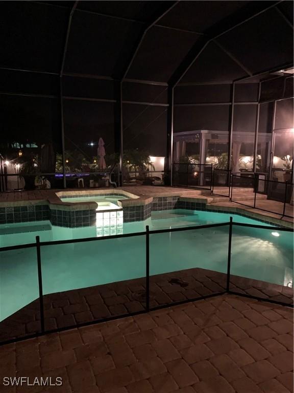 pool at night with an in ground hot tub, a patio, and a lanai