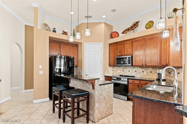 kitchen with brown cabinets, stainless steel appliances, light tile patterned flooring, a sink, and dark stone counters