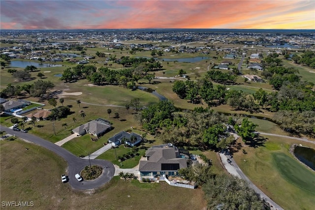 aerial view at dusk featuring golf course view, a water view, and a residential view