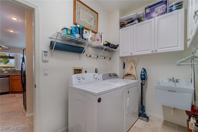 clothes washing area featuring light tile patterned floors, sink, washing machine and clothes dryer, and cabinets