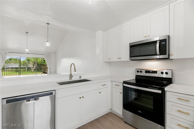 kitchen featuring stainless steel appliances, vaulted ceiling, white cabinets, hanging light fixtures, and sink