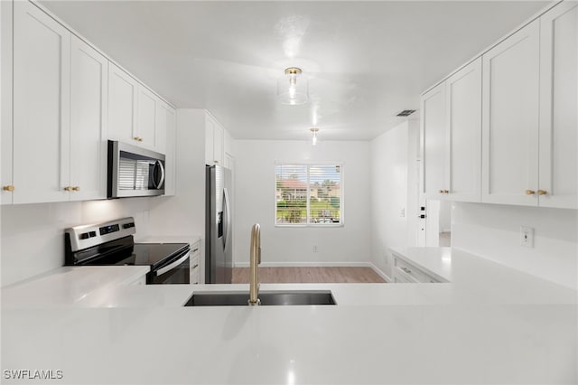 kitchen with white cabinets, light wood-type flooring, stainless steel appliances, and sink