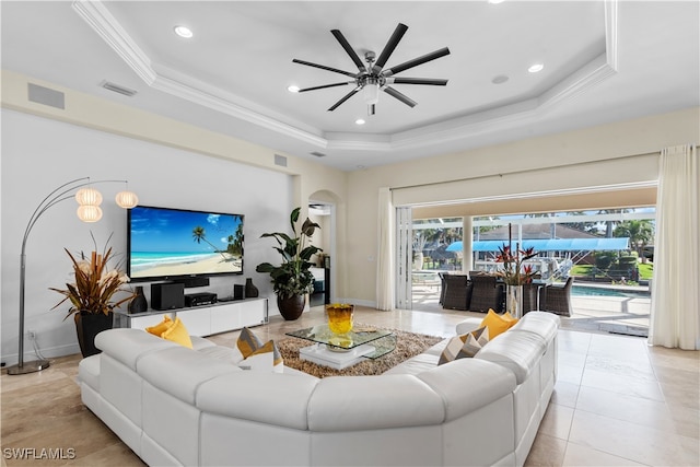 living room with light tile patterned flooring, ceiling fan, a tray ceiling, and crown molding