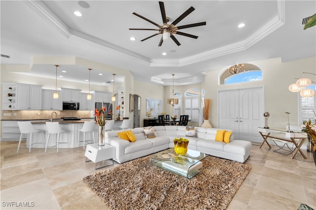 living room with sink, ornamental molding, a raised ceiling, and ceiling fan with notable chandelier