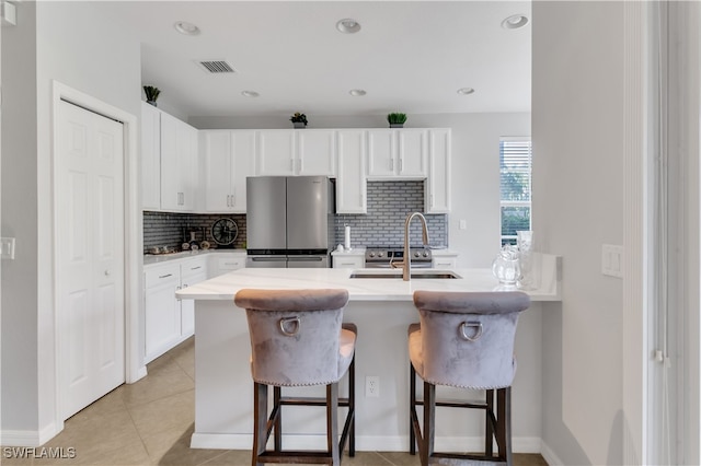 kitchen featuring white cabinetry, a breakfast bar area, backsplash, a kitchen island with sink, and stainless steel fridge