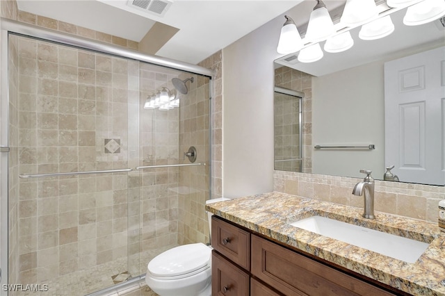 bathroom with vanity, toilet, a shower with door, and tasteful backsplash