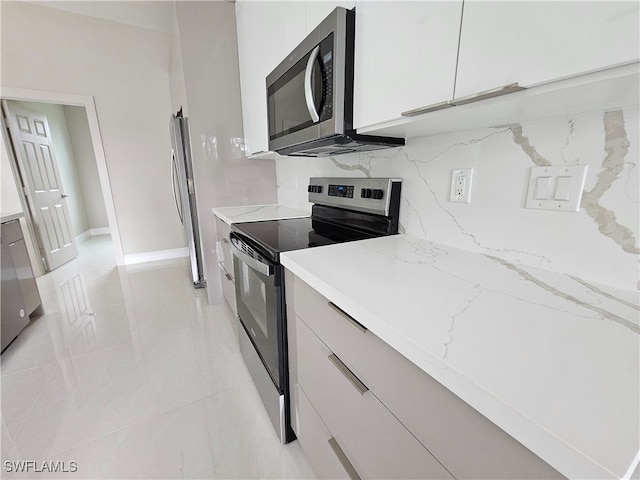 kitchen with stainless steel appliances, light stone countertops, white cabinets, and light tile patterned floors