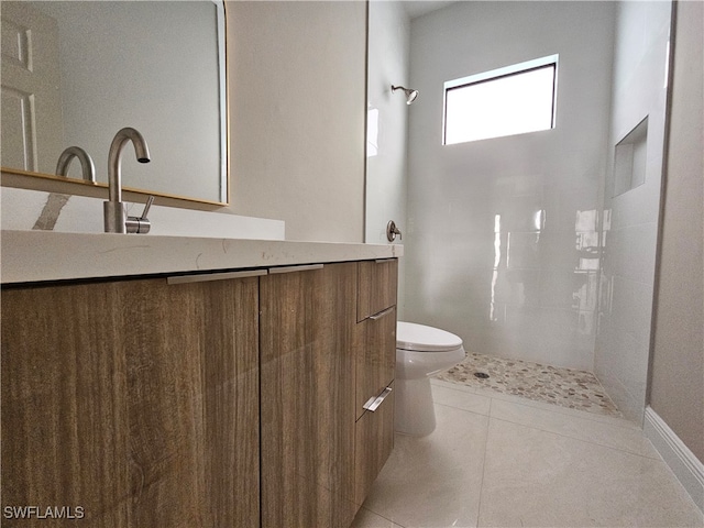 bathroom featuring toilet, a tile shower, vanity, and tile patterned floors