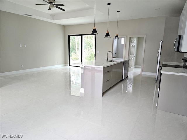 kitchen featuring stainless steel appliances, a center island with sink, sink, a tray ceiling, and pendant lighting