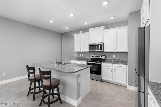 kitchen with a kitchen island with sink, dark stone counters, white cabinets, sink, and stainless steel appliances