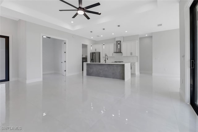 kitchen with a center island with sink, stainless steel refrigerator with ice dispenser, sink, white cabinets, and wall chimney exhaust hood