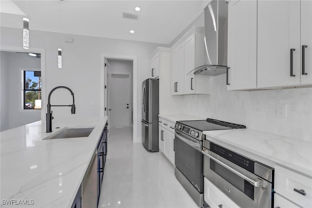 kitchen featuring white cabinets, appliances with stainless steel finishes, wall chimney range hood, and light stone countertops