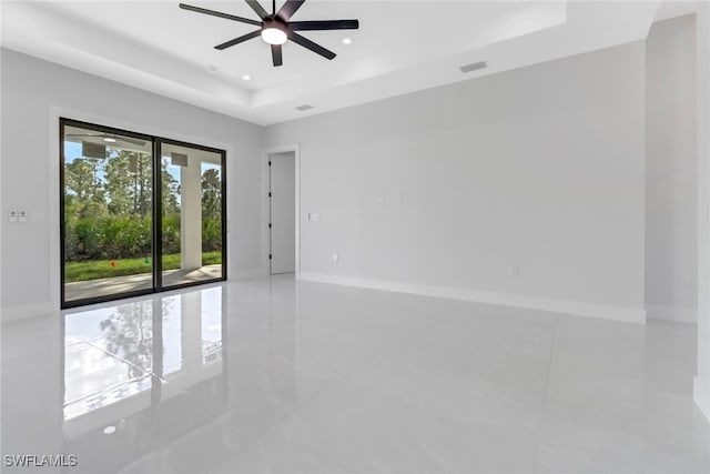 empty room with ceiling fan and a raised ceiling