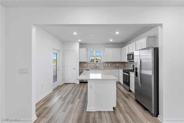 kitchen with light hardwood / wood-style floors, white cabinetry, sink, appliances with stainless steel finishes, and a kitchen island