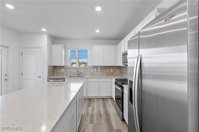 kitchen with stainless steel appliances, light stone counters, sink, white cabinetry, and light hardwood / wood-style flooring