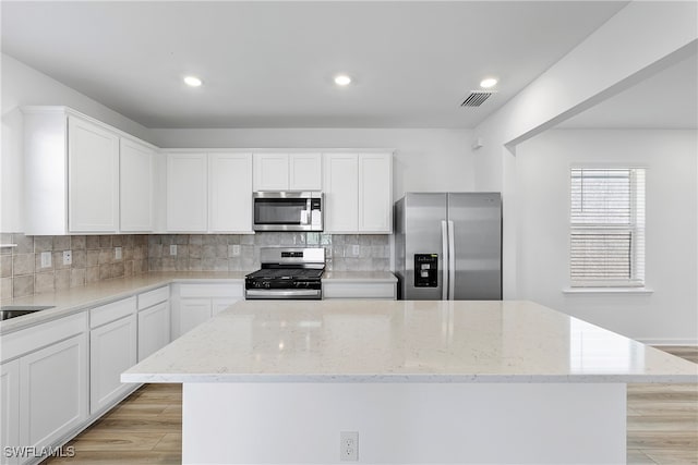 kitchen with white cabinetry, light wood-type flooring, appliances with stainless steel finishes, and light stone counters