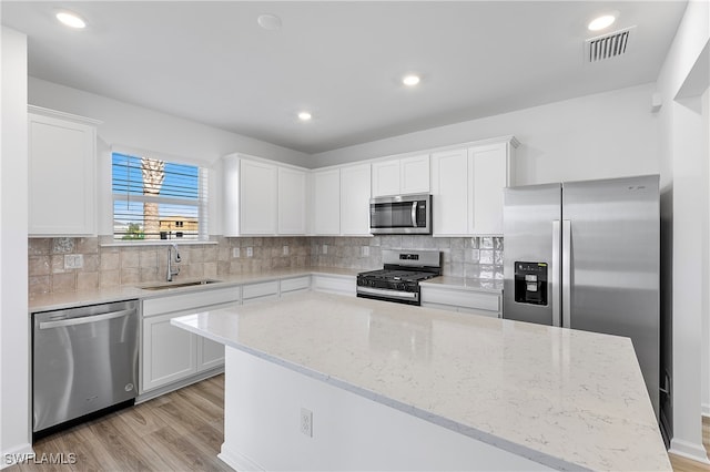 kitchen with white cabinetry, appliances with stainless steel finishes, sink, light hardwood / wood-style floors, and a center island