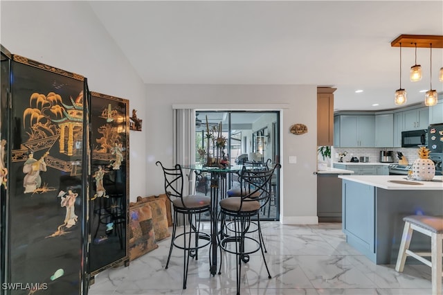 kitchen featuring a kitchen bar, backsplash, blue cabinetry, pendant lighting, and lofted ceiling