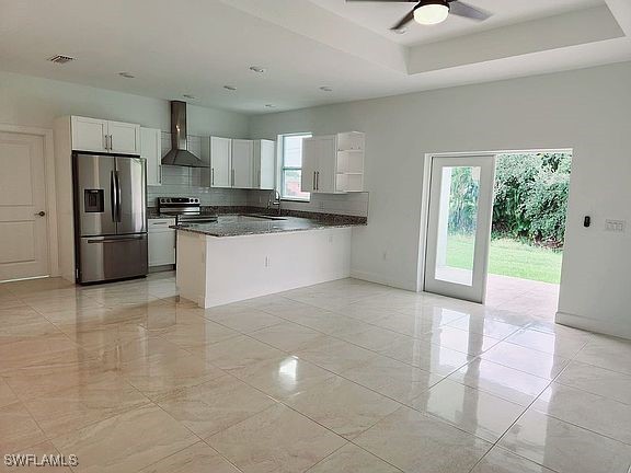 kitchen with white cabinets, stainless steel appliances, a healthy amount of sunlight, and wall chimney range hood