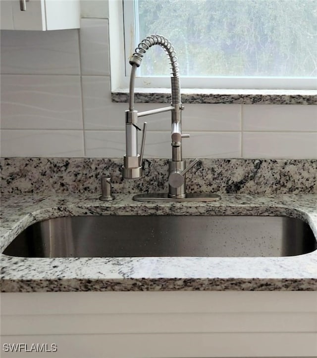 interior details featuring white cabinets, sink, and light stone counters