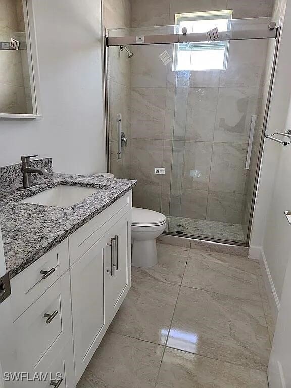 bathroom featuring toilet, vanity, an enclosed shower, and tile patterned floors