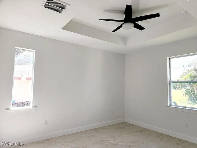 spare room featuring plenty of natural light, ceiling fan, and a raised ceiling