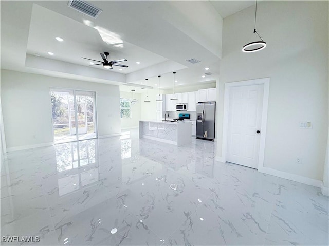 unfurnished living room featuring a tray ceiling, sink, and ceiling fan