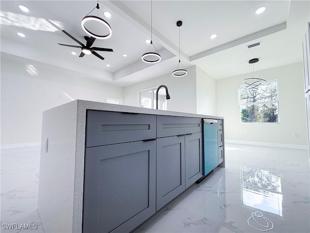 kitchen featuring a tray ceiling, a kitchen island, gray cabinetry, decorative light fixtures, and ceiling fan