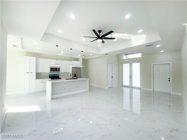 kitchen with white cabinets, an island with sink, appliances with stainless steel finishes, and a tray ceiling