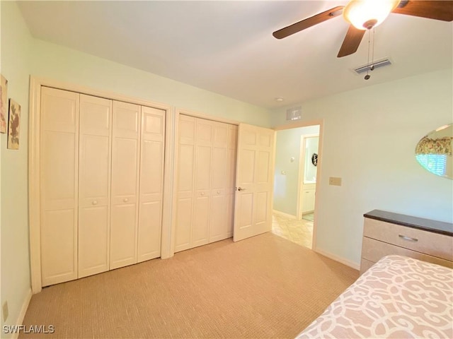 unfurnished bedroom with ceiling fan, light carpet, and multiple closets