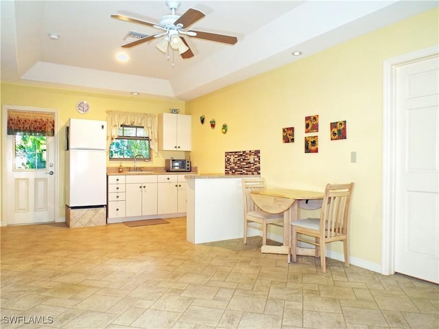 kitchen featuring white refrigerator, ceiling fan, a tray ceiling, white cabinetry, and kitchen peninsula