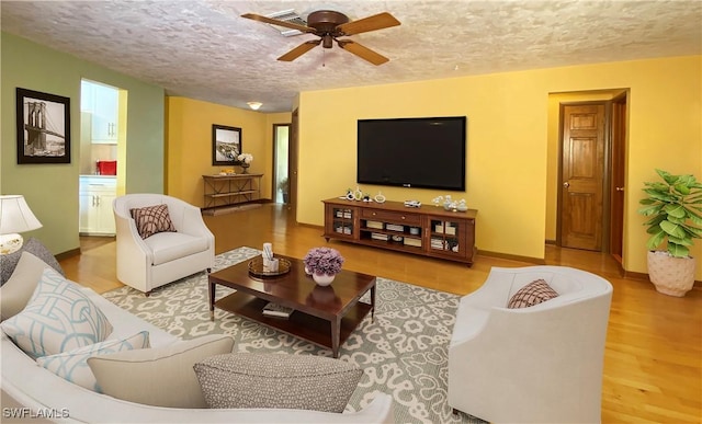 living room with ceiling fan, light hardwood / wood-style flooring, and a textured ceiling