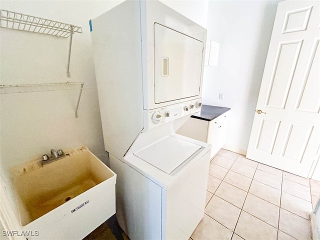 laundry area featuring light tile patterned floors, sink, and stacked washer / drying machine